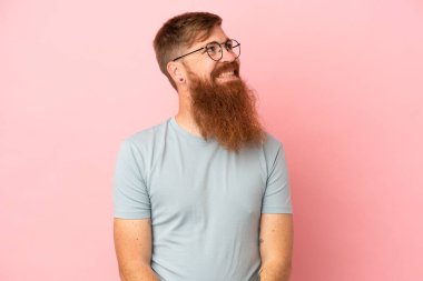 Pembe arka planda izole edilmiş genç beyaz adam yukarı bakarken bir fikir düşünüyor.