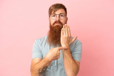 Pembe arka planda izole edilmiş genç beyaz adam geç kalma jesti yapıyor.