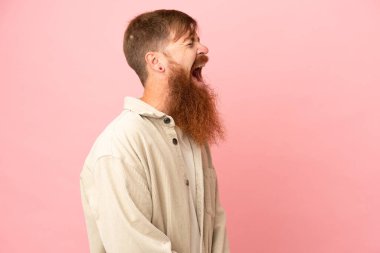 Kırmızımsı beyaz adam pembe arka planda izole edilmiş. Yan pozisyonda gülüyor.