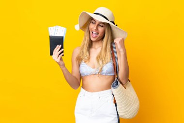 Mayolu genç Uruguaylı sarışın kadın bir zaferi kutlamak için izole edilmiş sarı bir arkaplanda pasaport taşıyor.