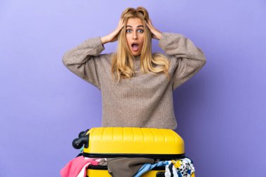 Genç Uruguaylı sarışın kadın, bir bavul dolusu elbisesiyle yalıtılmış mor duvarın üzerinde sürpriz bir ifadeyle.