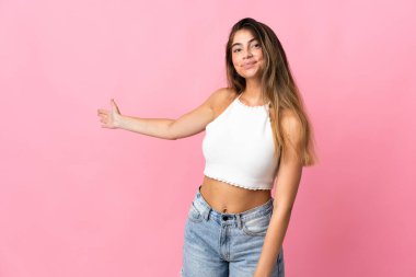 Pembe arka planda izole edilmiş genç beyaz kadın, davet edilmek için ellerini yana uzatıyor.