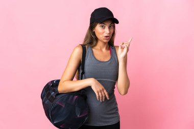 Spor çantalı genç bir kadın pembe arka planda izole edilmiş. Çözümü bulmak için parmağını kaldırıyor.