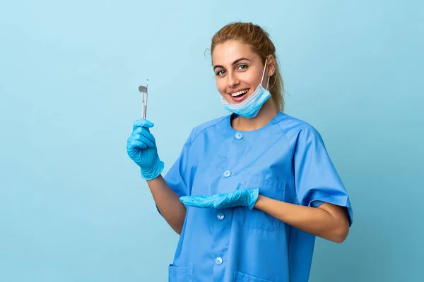 Młoda Kobieta Dentysta Trzyma Narzędzia Odizolowanym Niebieskim Tle Wyciągając Ręce — Zdjęcie stockowe