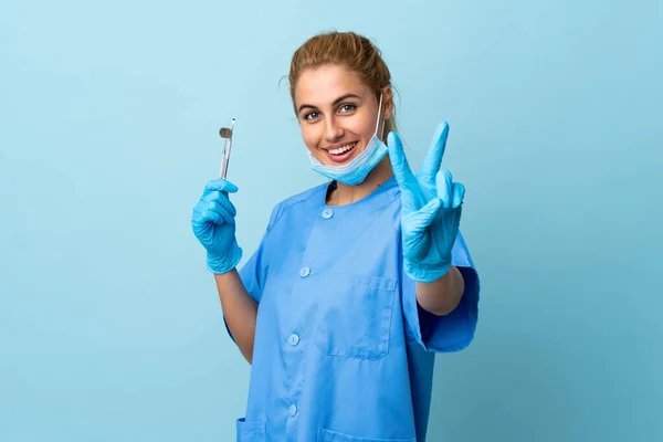 Mladá Žena Zubař Drží Nástroje Přes Izolované Modré Pozadí Úsměvem — Stock fotografie