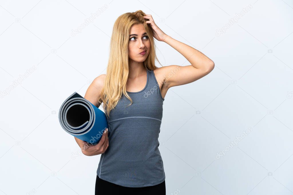 Young sport woman going to yoga classes while holding a mat over isolated white background having doubts and with confuse face expression