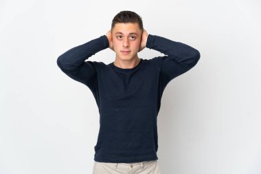 Beyaz arka planda izole edilmiş genç beyaz adam hayal kırıklığına uğramış ve kulaklarını kapatmış.