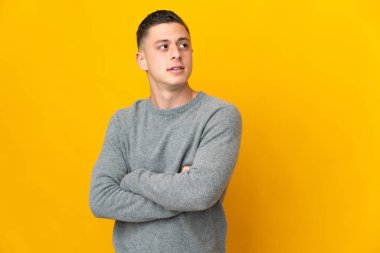 Sarı arka planda izole genç beyaz adam kollarını çapraz tutuyor.