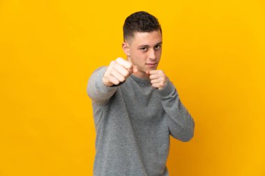 Kafkasyalı genç adam sarı arka planda yalıtılmış bir şekilde dövüşüyor.