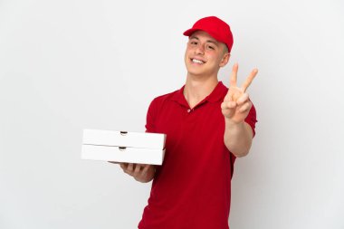 Pizza teslimatçısı üniformalı beyaz arka planda izole edilmiş pizza kutuları alıyor gülümsüyor ve zafer işareti gösteriyor.