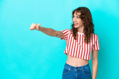 Mavi arka planda, kıvırcık saçlı genç bir kadın baş parmak hareketi yapıyor.