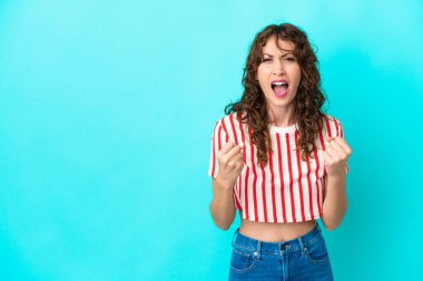 Mavi arka planda izole edilmiş kıvırcık saçlı genç bir kadın kötü bir durum yüzünden hayal kırıklığına uğradı.