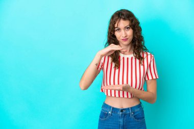 Mavi arka planda izole edilmiş kıvırcık saçlı genç bir kadın bir ilan vermek için avucunda hayali bir şey tutuyor.