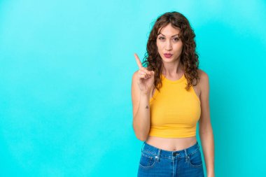 Mavi arka planda izole edilmiş kıvırcık saçlı genç bir kadın parmağını kaldırarak çözümü bulmaya çalışıyor.