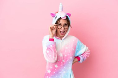 Tek boynuzlu at pijamalı beyaz bir kadın pembe arka planda gözlüklü ve şaşırmış.