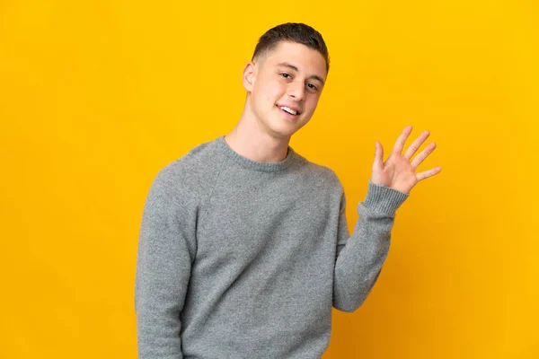 Jeune Homme Caucasien Isolé Sur Fond Jaune Saluant Main Avec — Photo