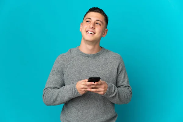 Ung Kaukasisk Man Isolerad Blå Bakgrund Med Hjälp Mobiltelefon Och — Stockfoto