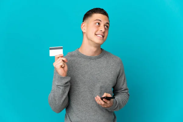 Νεαρός Καυκάσιος Άνδρας Απομονωμένος Μπλε Φόντο Αγοράζει Κινητό Πιστωτική Κάρτα — Φωτογραφία Αρχείου