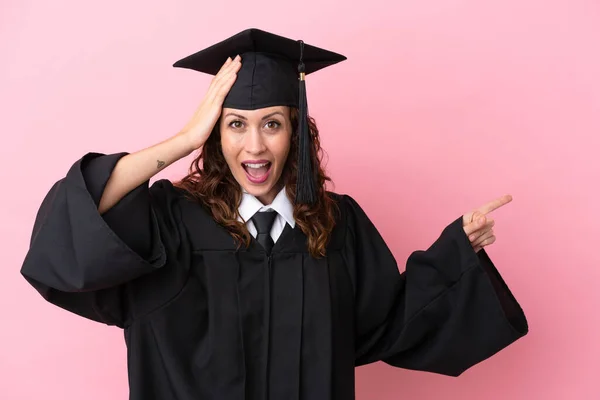 Joven Graduada Universitaria Aislada Sobre Fondo Rosa Sorprendida Señalando Con — Foto de Stock
