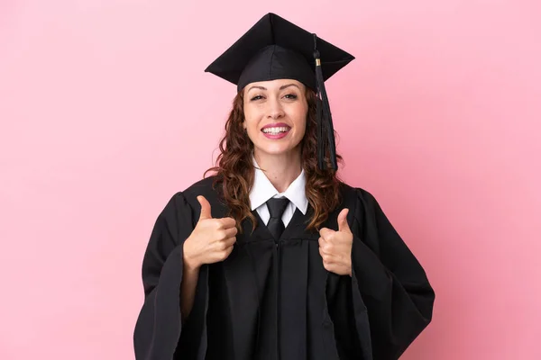 若いです大学院生女性隔離上のピンクの背景に親指アップジェスチャーと笑顔 — ストック写真