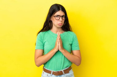 Sarı arka planda izole edilmiş genç beyaz kadın avuç içlerini bir arada tutuyor. İnsan bir şey ister.