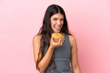 Pembe arka planda izole edilmiş beyaz bir kadın elinde donut tutuyor.