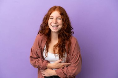 Genç, kızıl saçlı, soyutlanmış, mor arka planda gülümseyen bir kız.