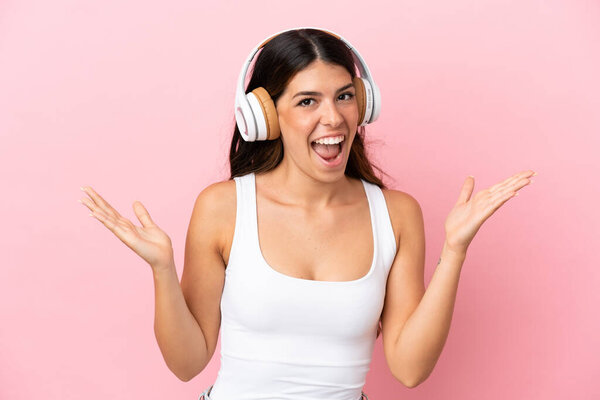Young caucasian woman isolated on pink background surprised and listening music