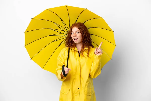 十代の若者たちRedhead女の子雨防止コートと傘隔離上の白い背景に実現しようとして解決策を持ち上げながら指アップ — ストック写真