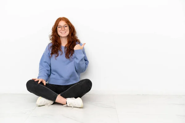 Teenager Zrzka Dívka Sedí Podlaze Izolované Bílém Pozadí Ukazuje Stranu — Stock fotografie