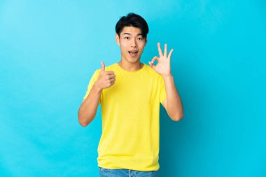 Mavi arka planda izole edilmiş genç bir Çinli işaret ve işaret işareti gösteriyor.