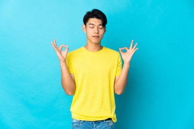 Zen pozisyonunda mavi arka planda izole edilmiş genç bir Çinli.