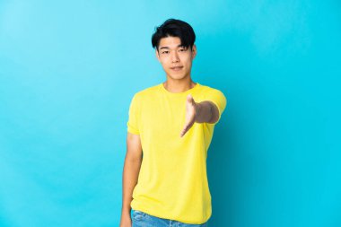 Mavi arka planda izole edilmiş genç bir Çinli iyi bir anlaşma için el sıkışıyor.