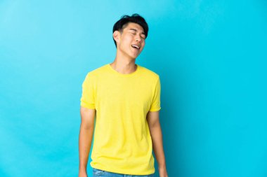 Genç Çinli adam mavi arka planda yalnız gülüyor.
