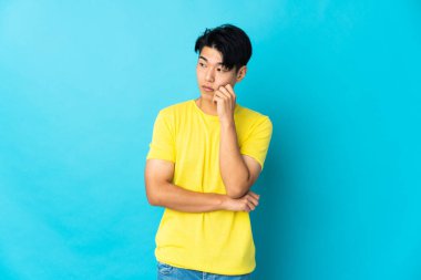 Genç Çinli adam mavi arka planda izole edilmiş, yorgun ve sıkılmış bir ifadeyle.