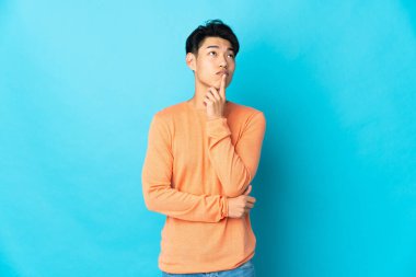 Genç Çinli bir adam mavi arka planda izole edildi.