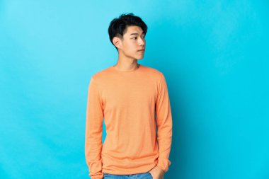 Mavi arka planda izole edilmiş genç bir Çinli yan tarafa bakıyor.