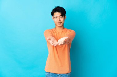 Genç Çinli bir adam mavi arka planda izole edilmiş. Kopyalama alanı hayali bir ilan vermek için avucunun içinde duruyor.