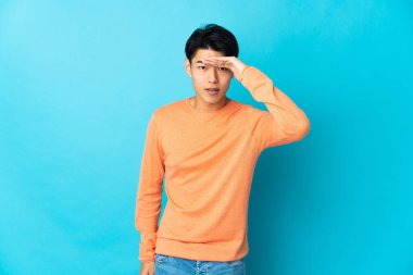 Genç Çinli bir adam mavi arka planda izole edilmiş. Bir şeye bakmak için çok uzaklara bakıyor.