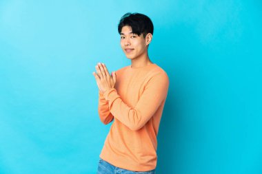 Genç Çinli bir adam mavi arka planda bir şeyler çeviriyor.