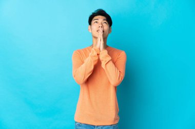 Mavi arka planda izole edilmiş genç bir Çinli avuç içlerini bir arada tutuyor. İnsan bir şey ister.