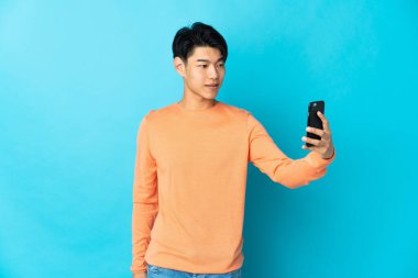 Mavi arka planda izole edilmiş genç bir Çinli selfie çekiyor.