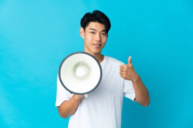 Mavi arka planda izole edilmiş genç bir Çinli. Elinde baş parmağıyla bir megafon tutuyor.