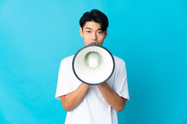 Mavi arka planda izole edilmiş genç bir Çinli megafonla bir şey duyurmak için bağırıyor.