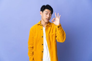 Mor arka planda izole edilmiş genç bir Çinli parmaklarıyla işaret veriyor.