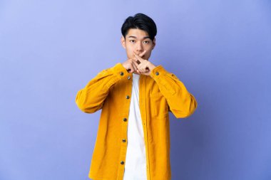 Mor arka planda izole edilmiş genç bir Çinli sessizlik işareti gösteriyor.