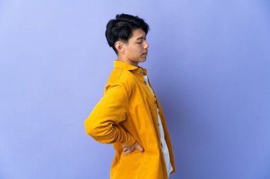 Genç Çinli bir adam mor arka planda izole edilmiş. Çaba gösterdiği için sırt ağrısı çekiyor.