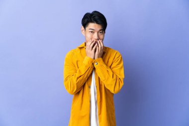 Mor arka planda izole edilmiş genç bir Çinli mutlu ve gülümseyen elleriyle ağzını kapatıyor.