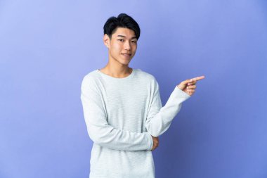 Mor arka planda izole edilmiş genç Çinli adam, parmağını yana doğru gösteriyor.