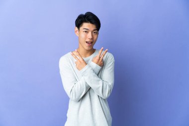 Mor arka planda izole edilmiş genç Çinli adam gülümsüyor ve zafer işareti gösteriyor